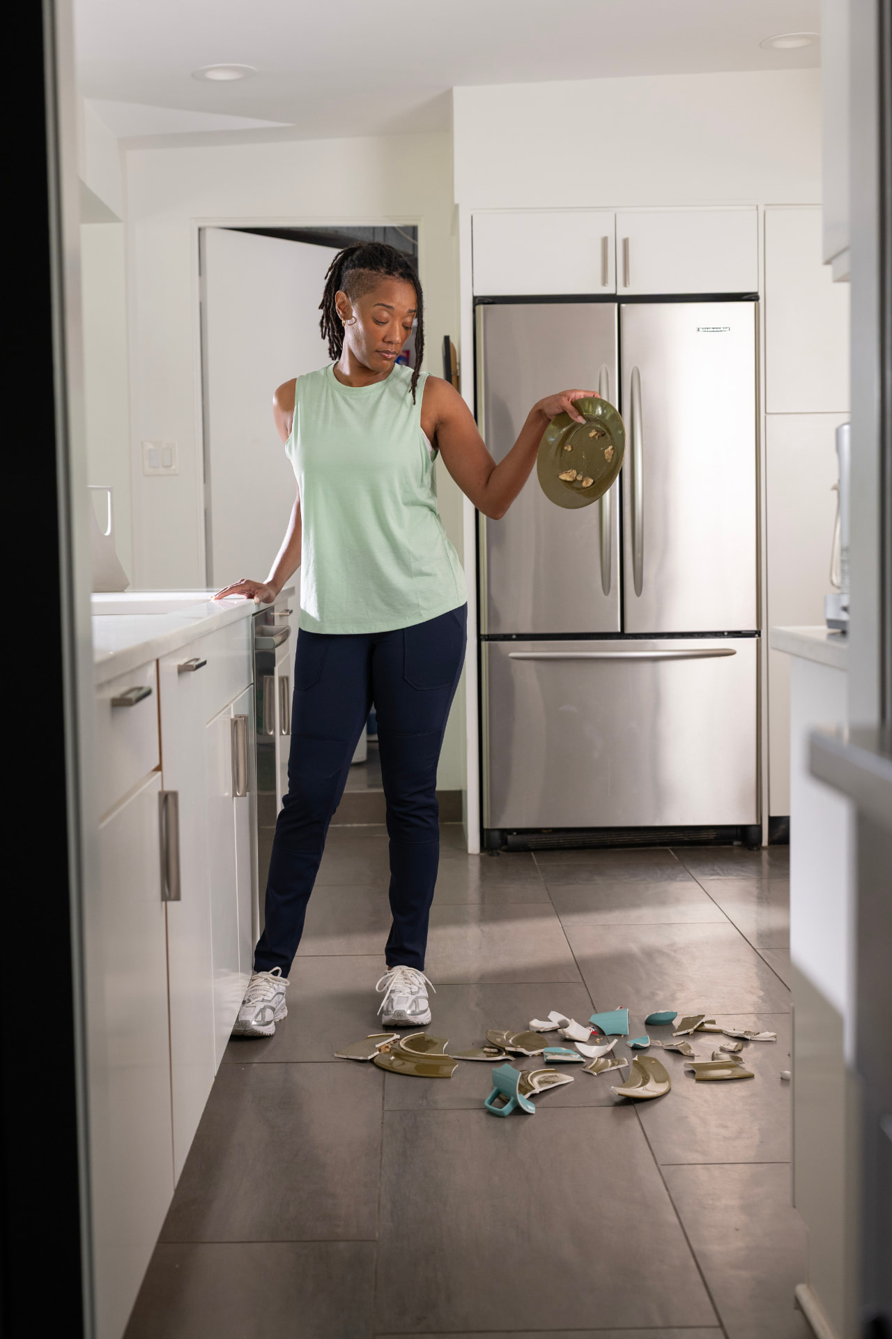 A woman standing over broken dishes on the floor